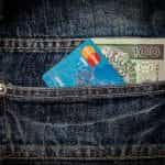 Tarjeta Mastercard y un billete de 100 sobresaliendo de bolsillo trasero de un pantalón.