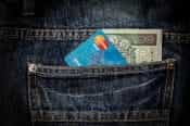 Tarjeta Mastercard y un billete de 100 sobresaliendo de bolsillo trasero de un pantalón.