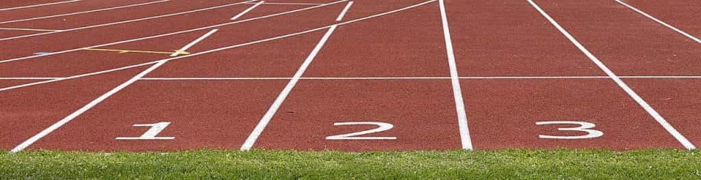 El inicio de las tres primeras pistas de carreras en un hipódromo, con suelo rojo y los números en blanco.