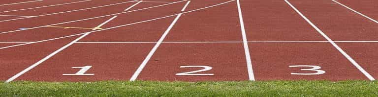 El inicio de las tres primeras pistas de carreras en un hipódromo, con suelo rojo y los números en blanco.