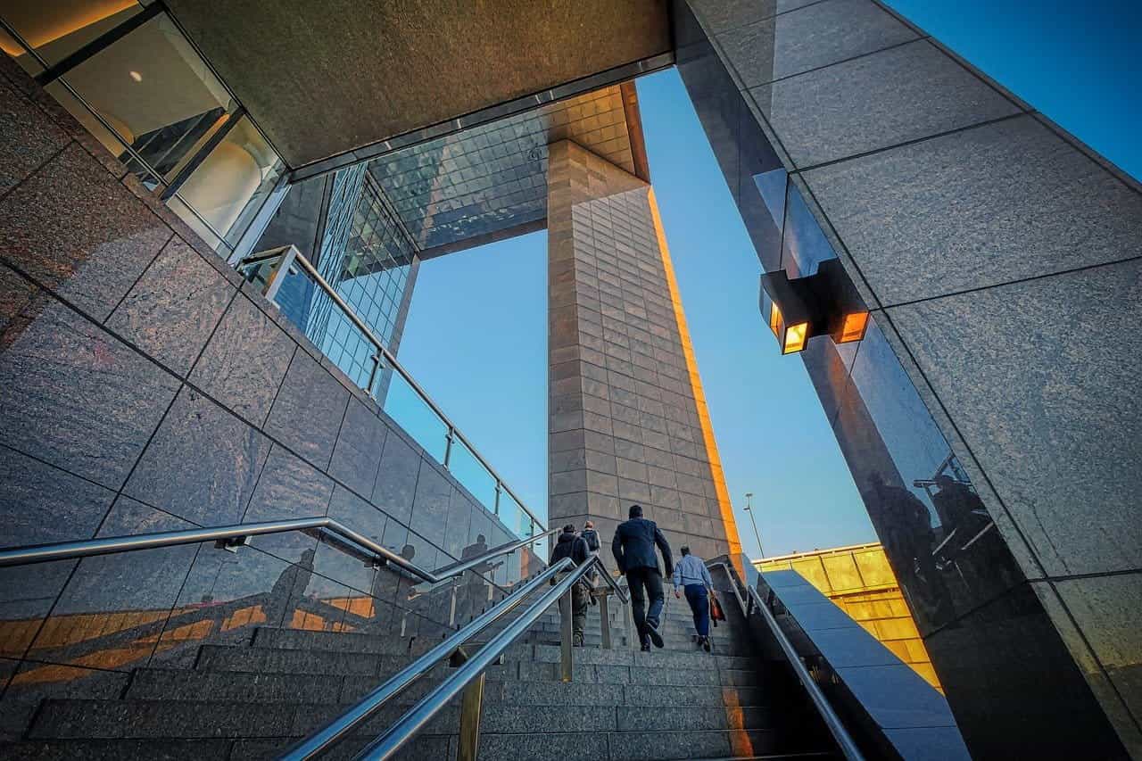 Personas de vestimenta formal suben las escalinatas de un edificio corporativo.