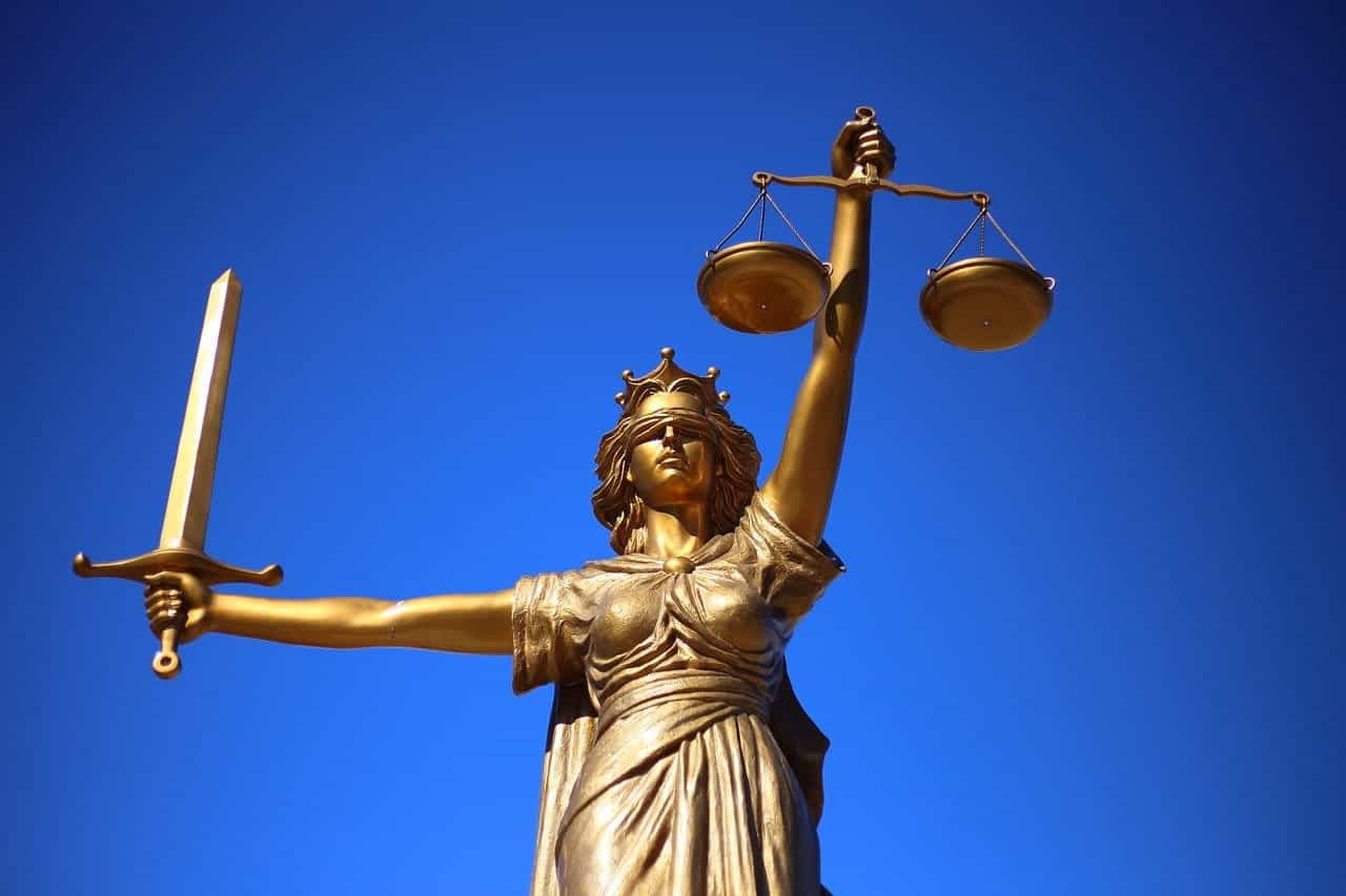 Estatua de la justicia con ojos vendados, balanza en alto en mano izquierda y espada en mano derecha.