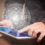 Bola luminosa de líneas y nodos emergiendo de una tablet operada por persona con manos blancas y atuendo formal.