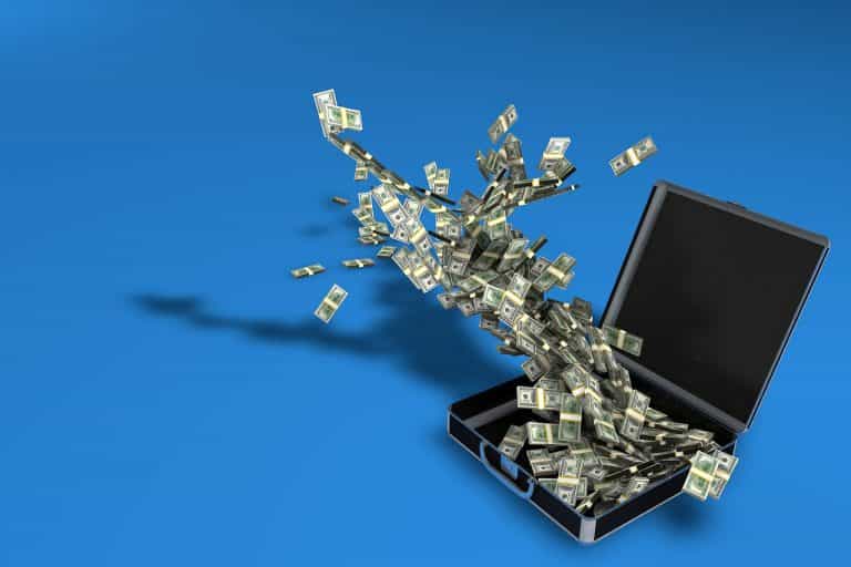 Maletín abierto con billetes de dólar volando fuera de él.