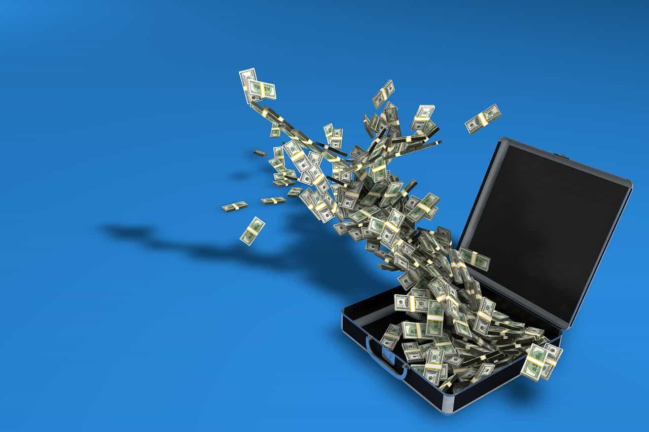 Maletín abierto con billetes de dólar volando fuera de él.