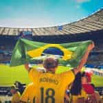 Persona de espaldas con la camiseta de Robinho en un estadio de fútbol levantando la bandera de Brasil.