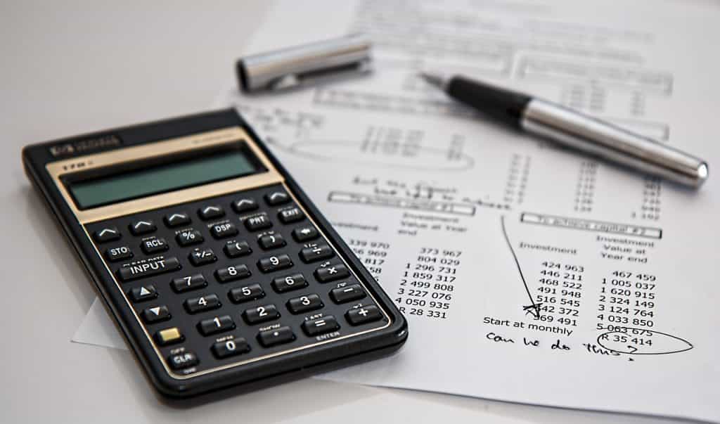 Calculadora junto a bolígrafo sobre un papel con cuentas y anotaciones.