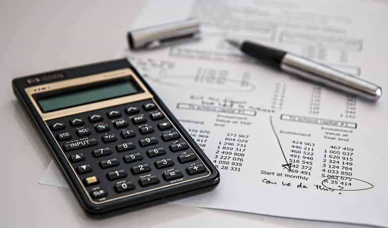Calculadora junto a bolígrafo sobre un papel con cuentas y anotaciones.