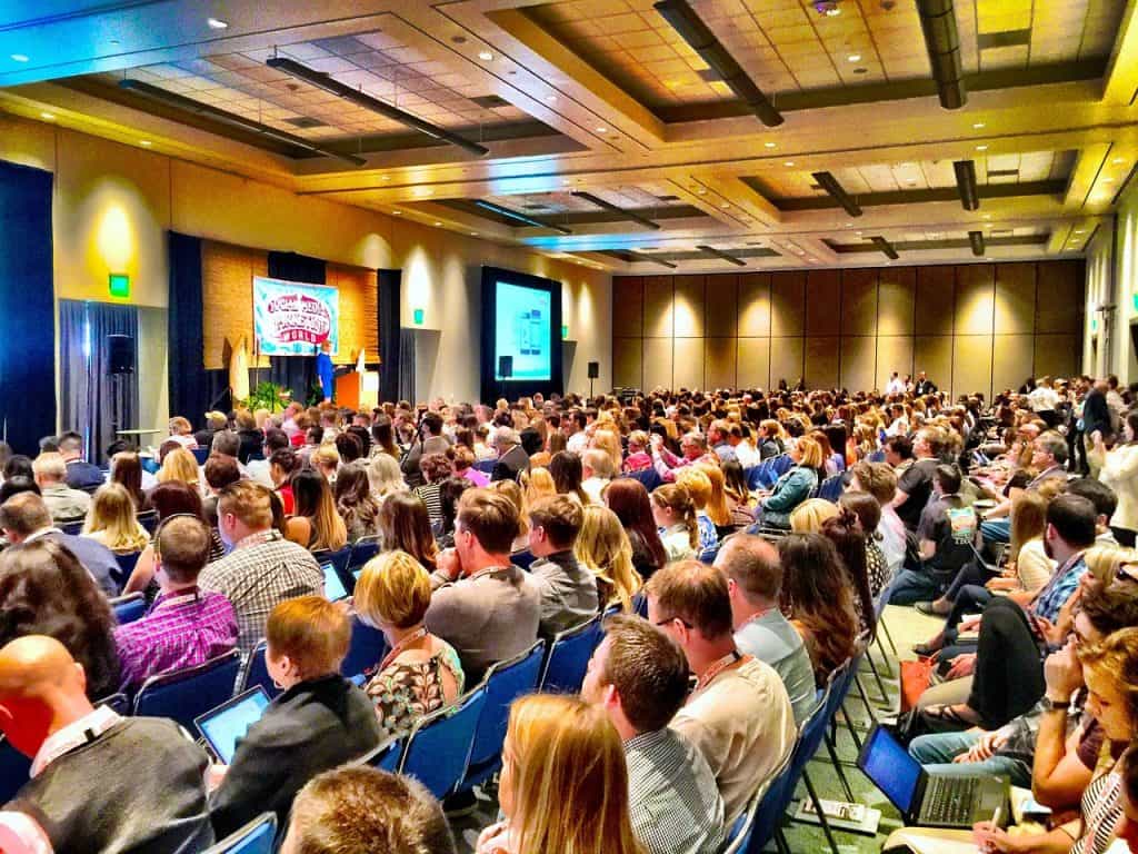 Gran cantidad de personas sentadas atendiendo a una conferencia en una sala de eventos.