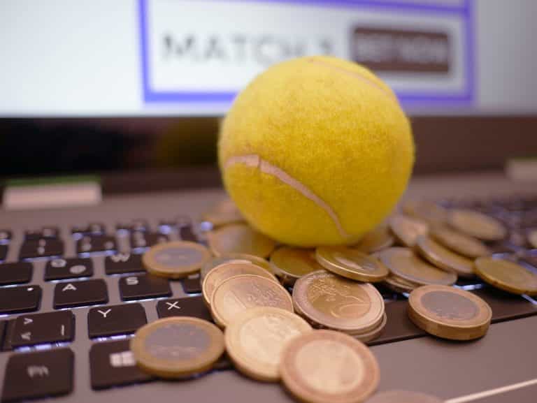 Monedas y una pelota de tenis sobre el teclado de un ordenador portátil.