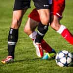 Dos jugadores de fútbol trabando las rodillas para disputar la pelota.