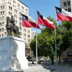 Plaza en Santiago de Chile, con un monumento de hombre a caballo y tres banderas del país ondeando desde sus respectivos mástiles.