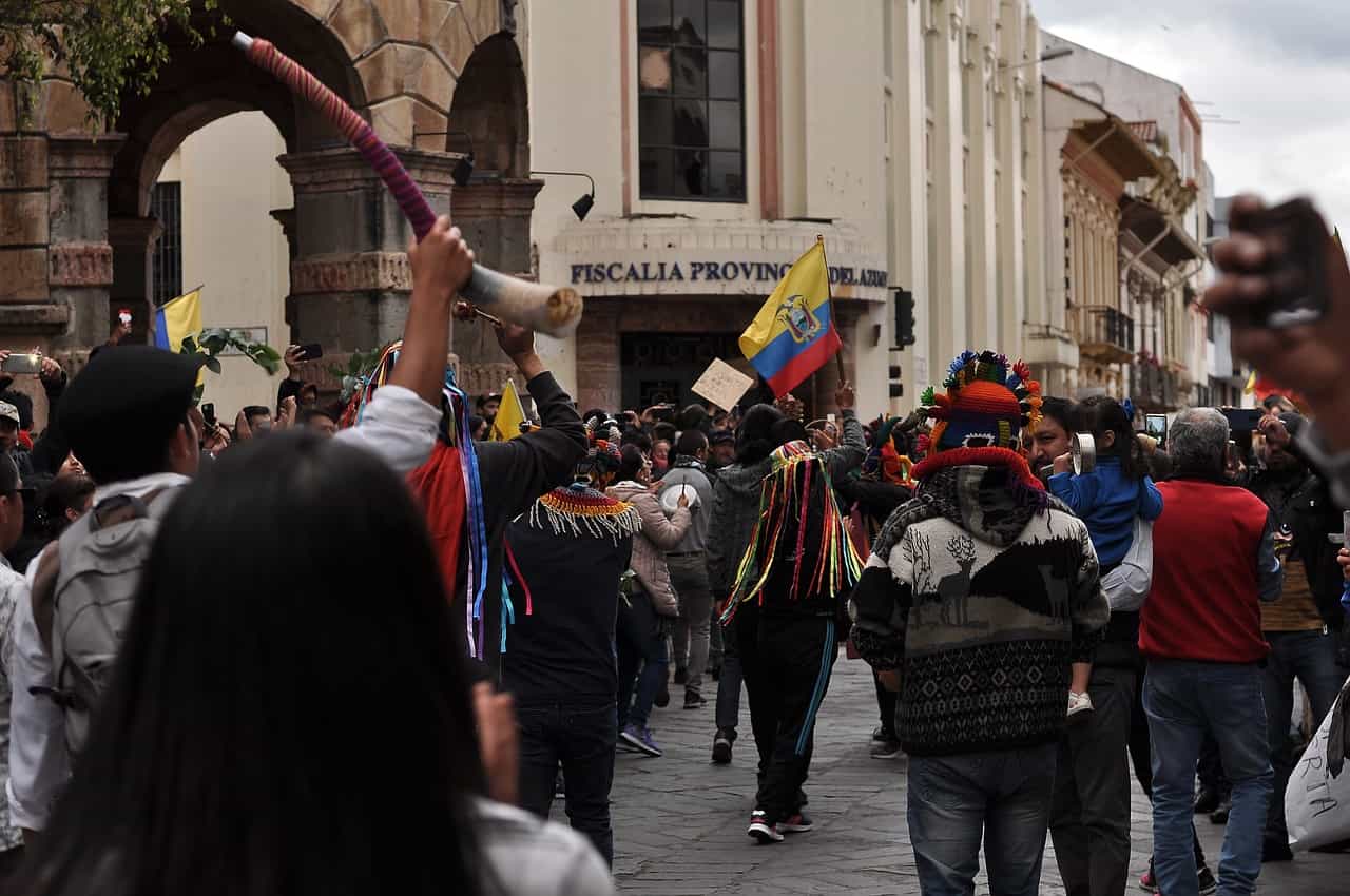 Protesta social en Ecuador, gente marchando con banderas y cuernos.