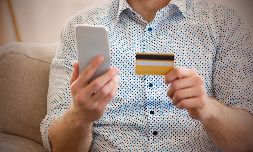 Persona con un teléfono móvil en la mano y una tarjeta bancaria.