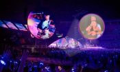 Pantalla gigante en concierto con pareja destacada por la Kiss Cam y público iluminado.