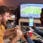 Hombres celebran una apuesta deportiva mientras ven un partido de fútbol en la televisión