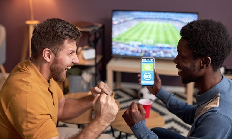 Hombres celebran una apuesta deportiva mientras ven un partido de fútbol en la televisión