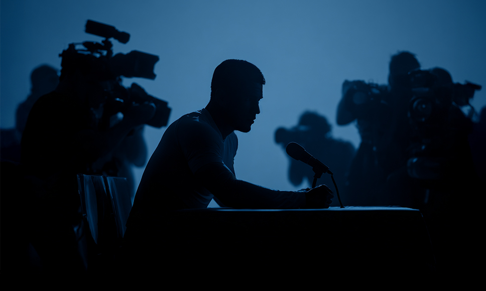 Silueta de un hombre sentado ante un micrófono durante una rueda de prensa.