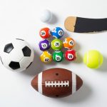 Balones deportivos, bolas de lotería y taco sobre fondo blanco.