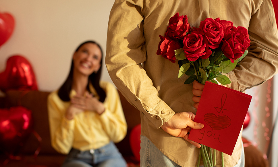 Hombre sosteniendo flores rojas y una tarjeta detrás de la espalda
