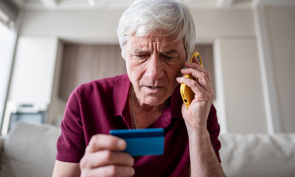Hombre mayor con teléfono en la mano y una tarjeta bancaria azul.