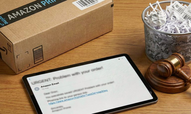 Caja de Amazon y tablet con correo sospechoso sobre una mesa, junto a papeles triturados.