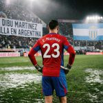 Portero de fútbol con camiseta número 23 frente a estadio y pancarta en gradas