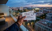 Mano sosteniendo entradas de fútbol Real Madrid vs Barcelona con ciudad al fondo