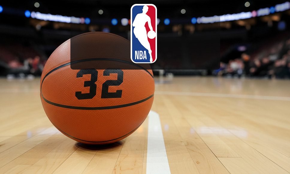 Un balón de baloncesto en una cancha con el logo de la NBA al fondo