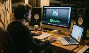 Hombre con auriculares trabajando en estudio musical frente a ordenador con Spotify