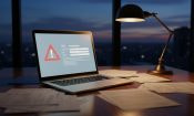 Un portátil con una alerta de seguridad en la pantalla sobre una mesa con documentos