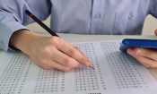 Estudiante rellenando una hoja de examen tipo test mientras consulta un teléfono móvil.