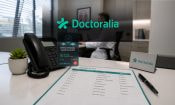 Teléfono de una consulta médica con una alerta de llamada sospechosa y un médico al fondo en su despacho