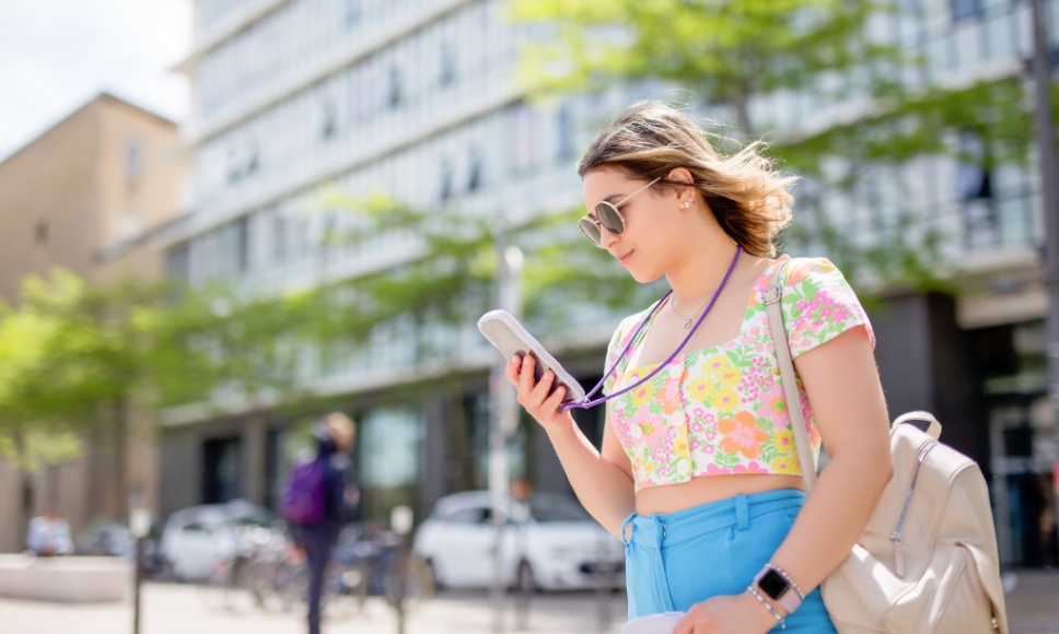 Mujer joven mira su móvil en la calle, un momento común en el que suelen colarse las estafas digitales.