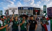 Aficionados frente a un estadio del Mundial 2026 usando el móvil junto a carteles sobre redes WiFi gratuitas y sospechosas.