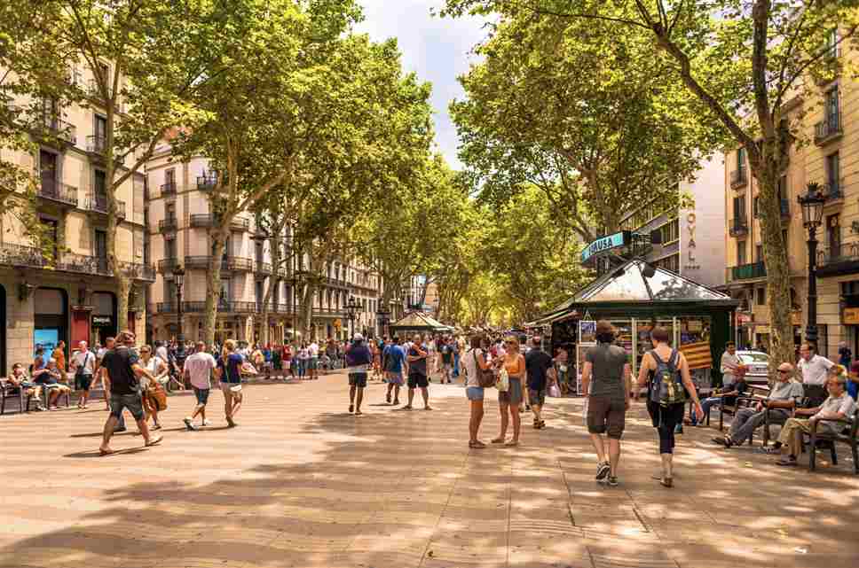 Turistas caminan por una zona concurrida de España con mochilas y bolsos.