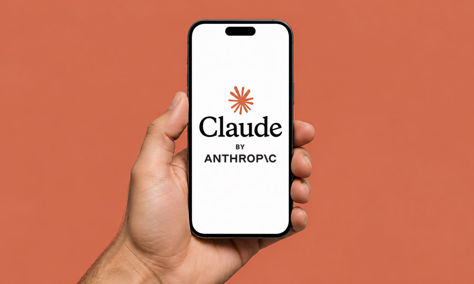 Mano sosteniendo un móvil con la pantalla de inicio de la app de Claude, de Anthropic, sobre fondo naranja.