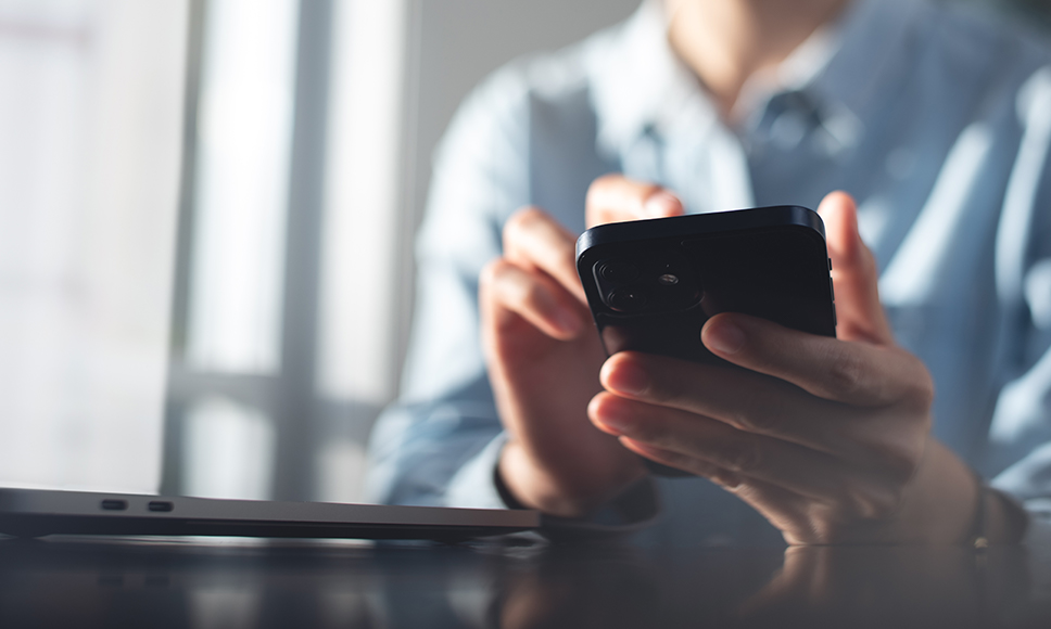 Persona con camisa de oficina sosteniendo su móvil, sobre el bloqueo de SMS bancarios con alias falso en España.