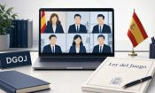 Videollamada de seis personas en un portátil junto a una placa DGOJ y un libro titulado Ley del Juego, con bandera española.