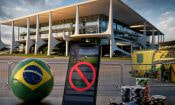 Balón con la bandera brasileña y fichas de casino ante el Palacio del Planalto, con un móvil mostrando una app de apuestas bloqueada.