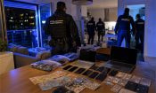 Agentes de la Policía Nacional en un registro nocturno con ordenadores, móviles y billetes incautados sobre una mesa.